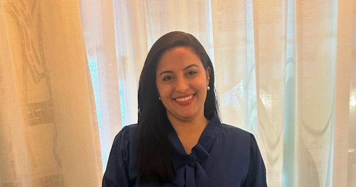 Patrícia Alencar sorrindo, em frente a cortinas claras